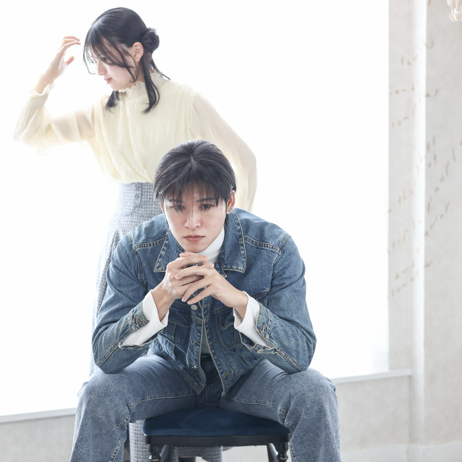 椅子に座って考え込むポーズの男性と後ろに女性